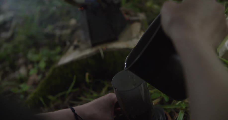 Person pouring liquid from a pot into a cylindrical container outdoors