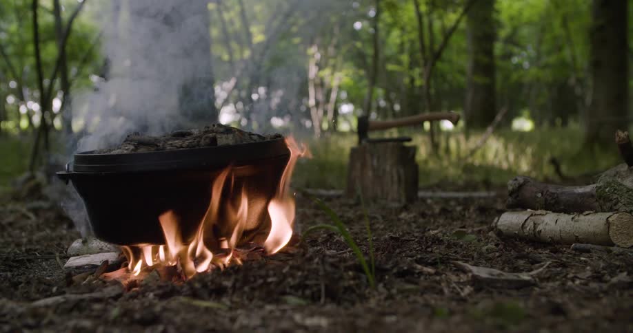 Pot heated by fire at a campsite on a forest floor
