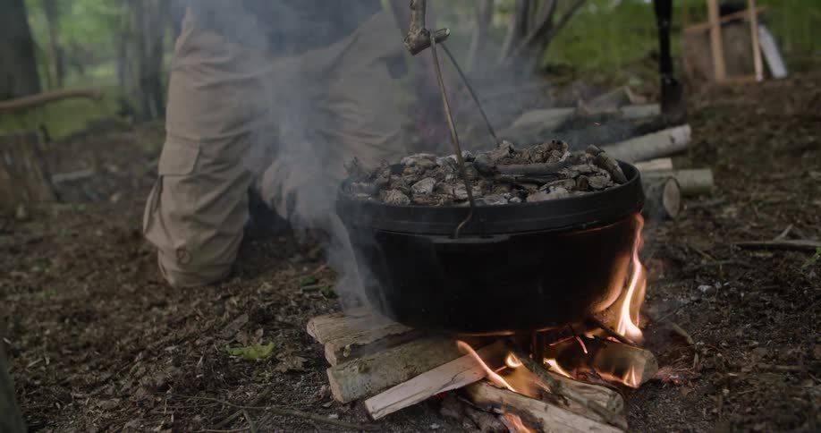 The man hangs the pot over the campfire