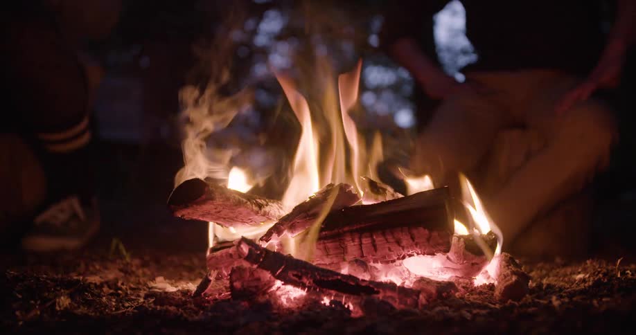 Close up of two people sitting around a campfire in a woodland at night