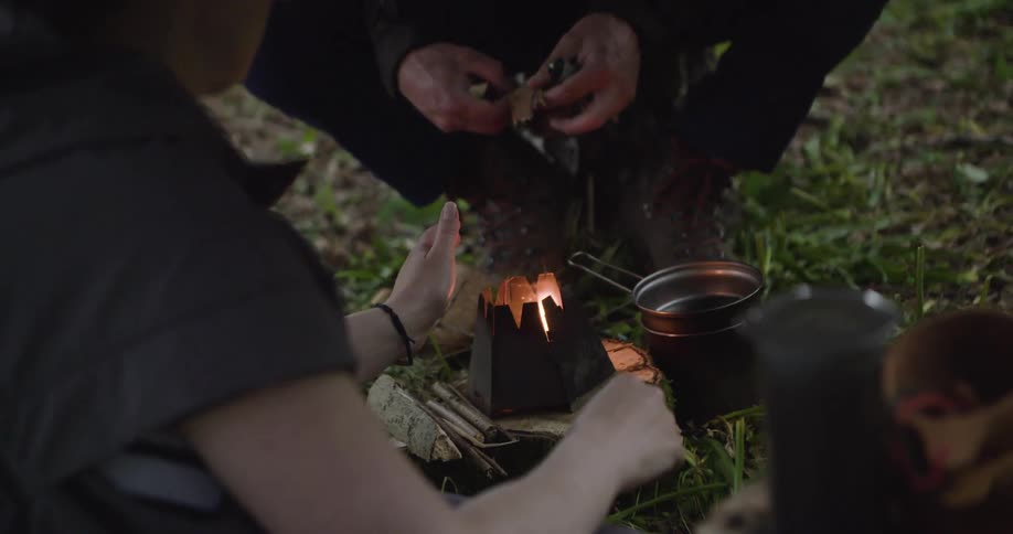 People lighting a small campfire on the ground covered with grass and leaves