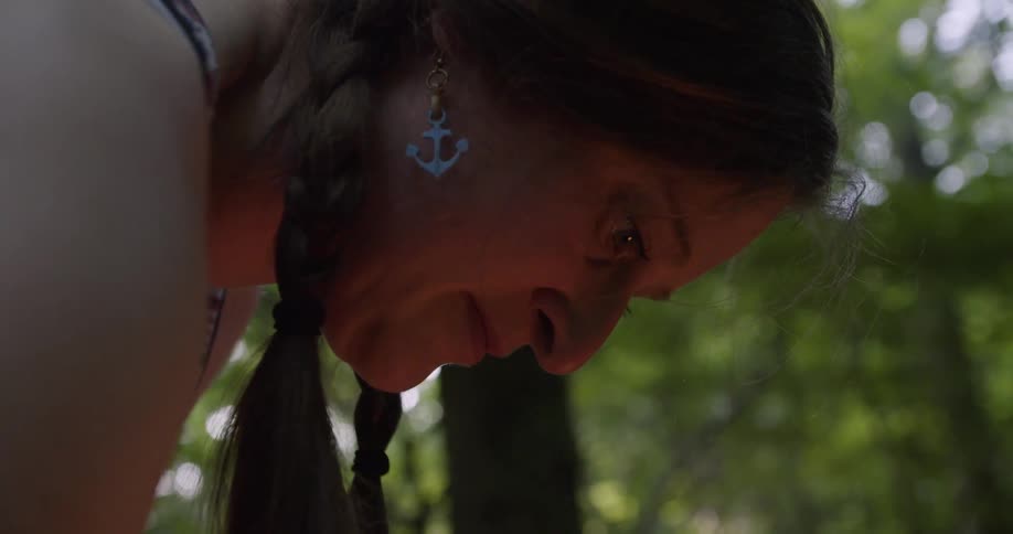 A middleaged woman sets up a campfire in the woods at midday carefully arranging the wood as sunlight filters through the trees