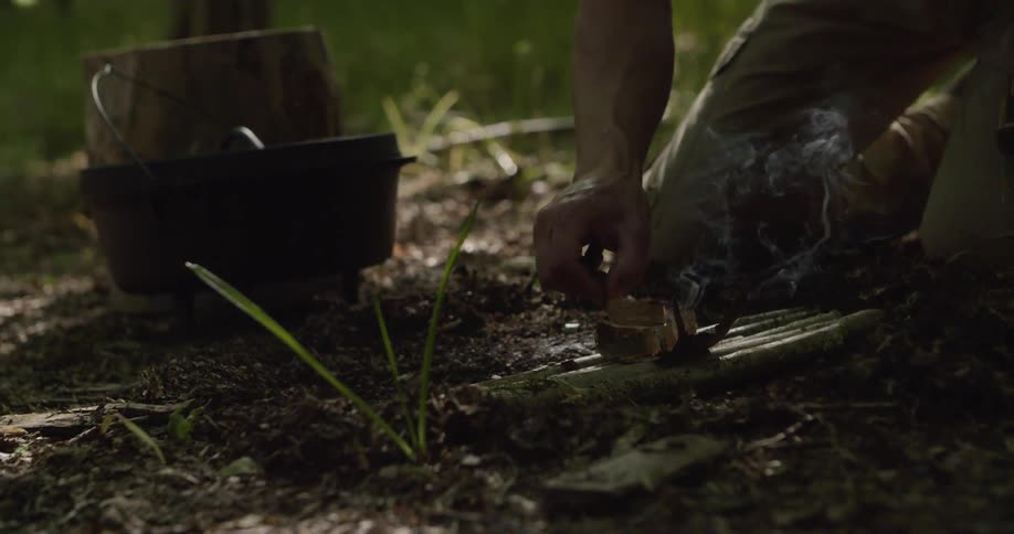 Close up of a young man making fire while kneeling in a woodland area during daytime