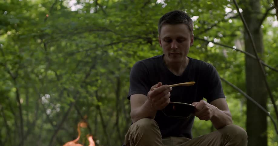 The man is eating by the campfire