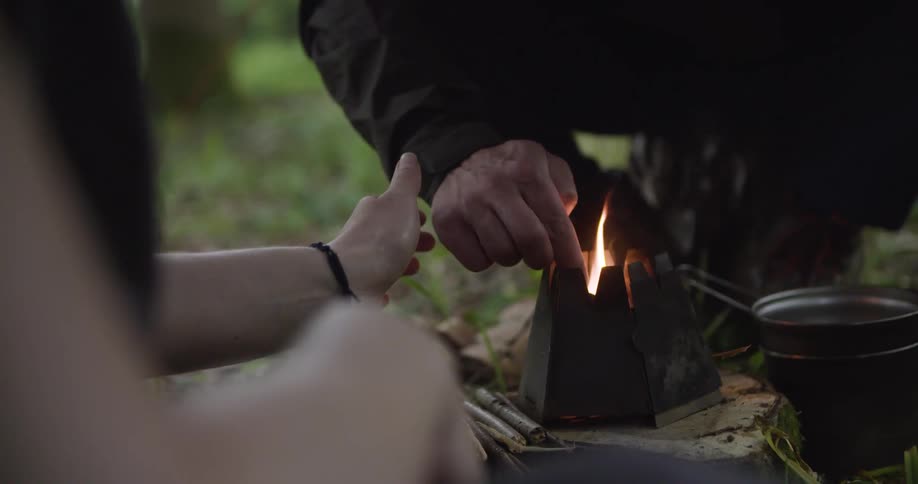People lighting a fire in a small stove set on the ground outdoors