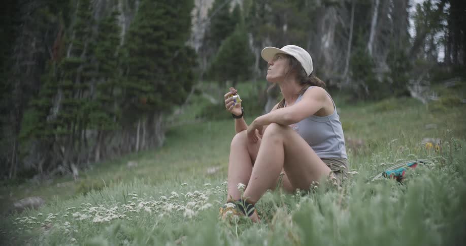 Woman sitting in a flowered field takes a snack break surrounded by nature