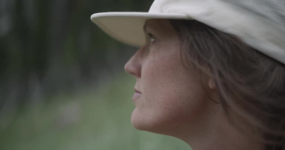A closeup shot of a woman wearing a white baseball cap set against a soft outoffocus background of green and dark foliage