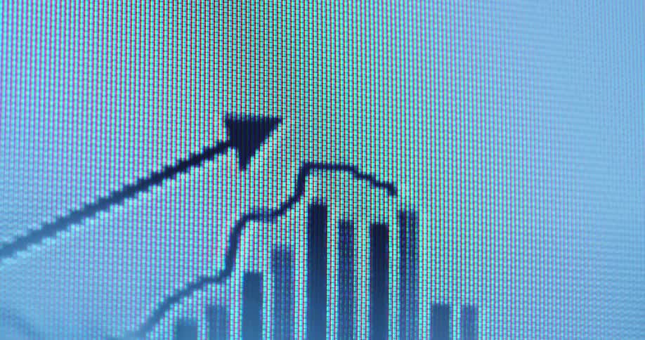 Macro close-up view of a digital screen shows an animated graph with a rising line chart and an upward pointing arrow overlaying vertical bar charts representing market growth or financial success on a white computer screen background