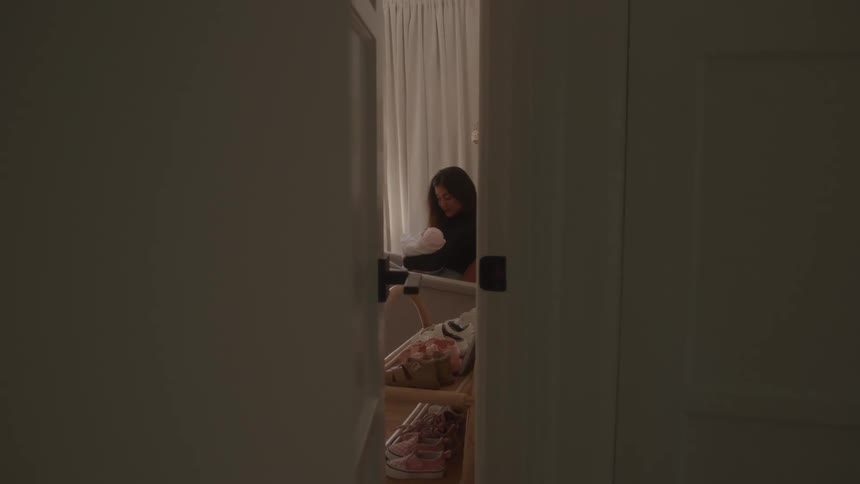 Partial view of a woman sitting in a room holding a baby wrapped in a light blanket