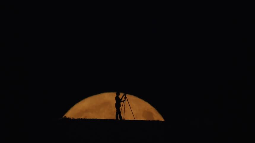 The man sets up a telescope to view the yellow moon