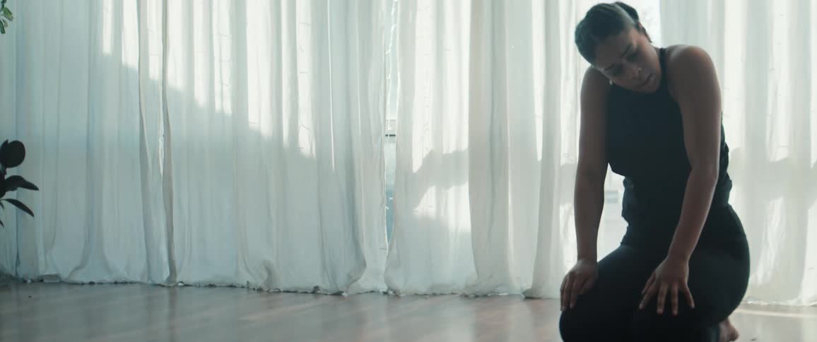 Woman in black clothing dancing on the floor with her body arched in a naturally lit space