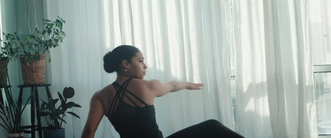 Woman in black clothing dancing seated on the floor of a naturally lit space