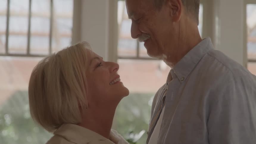 Mature couple gaze at each other with affectionate smiles in a bright setting
