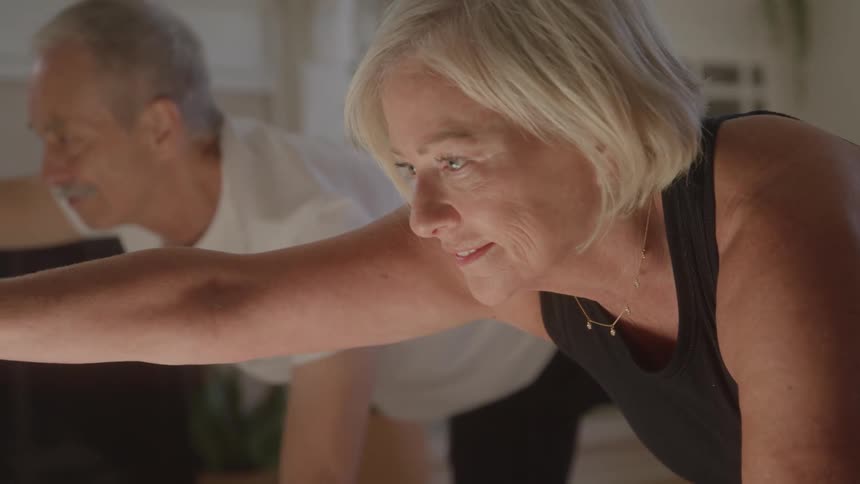 Close up of a middle aged couple stretching while doing yoga together in a living room during daytime