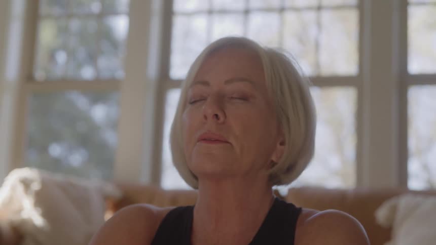 A woman wearing a black shirt sits on the floor indoors in deep meditation at midday