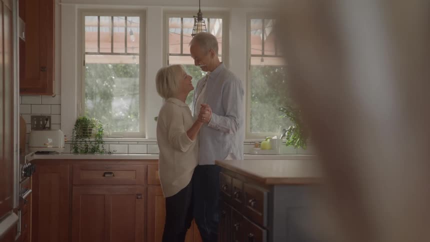 An elderly couple dancing together while standing in a kitchen during daytime