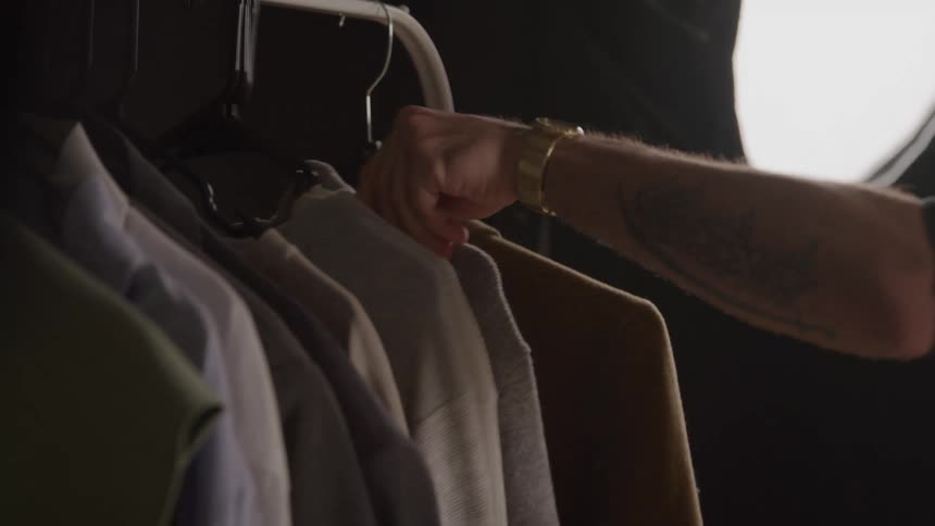 Male arm selects a piece among hanging clothes in a welllit studio