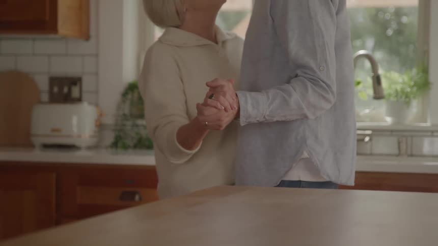 Couple dancing hand in hand in a kitchen lit by natural light