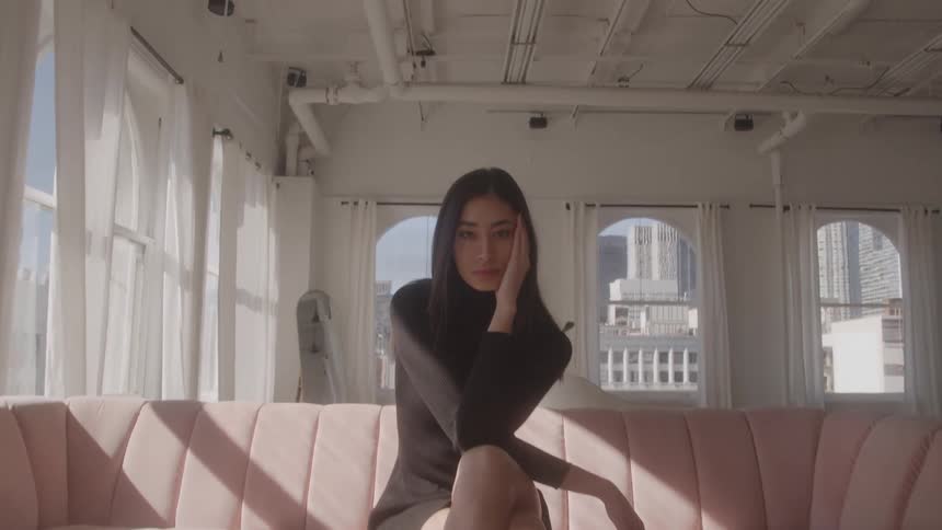 Woman sits on a pink sofa looking ahead with a thoughtful expression