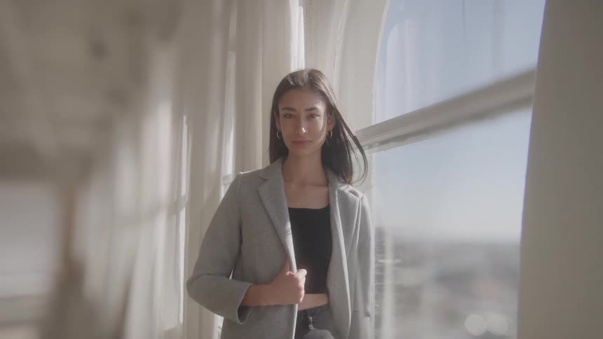 Young female model posing with a jacket next to a window indoors during day time