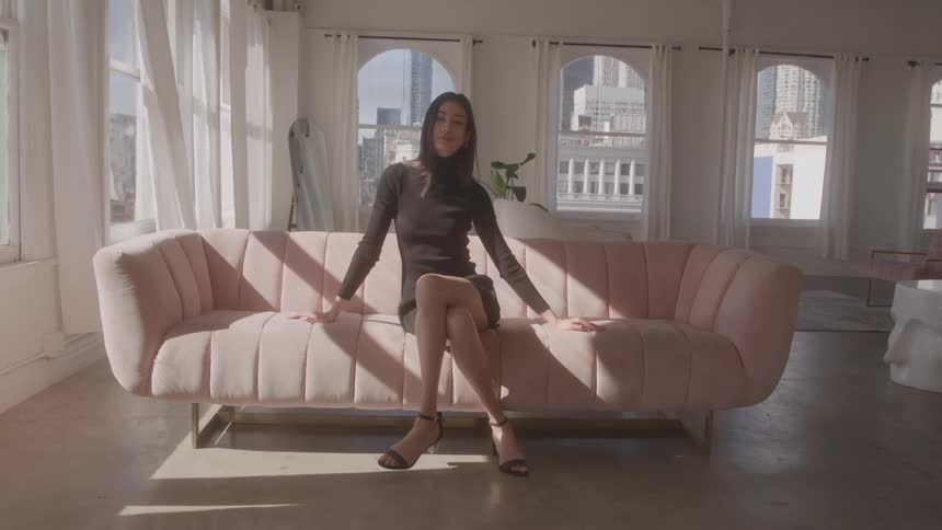 A young female model trying different poses while sitting on a couch in a room during daytime