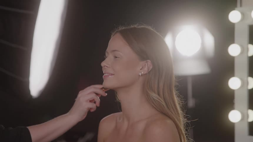Close up of a young woman getting face makeup in a lit studio