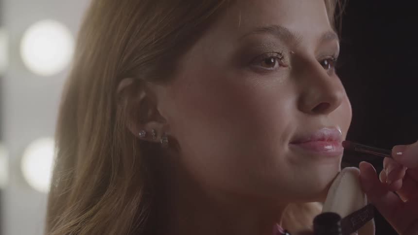 The makeup artist uses a brush to apply lipstick on the smiling model