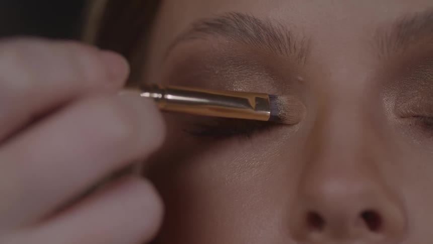 Close up of a makeup artist applying makeup to a young womans eyelids with a brush