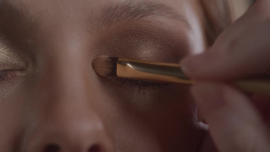 A persons eye as a makeup artist applies shimmering eyeshadow with a brush