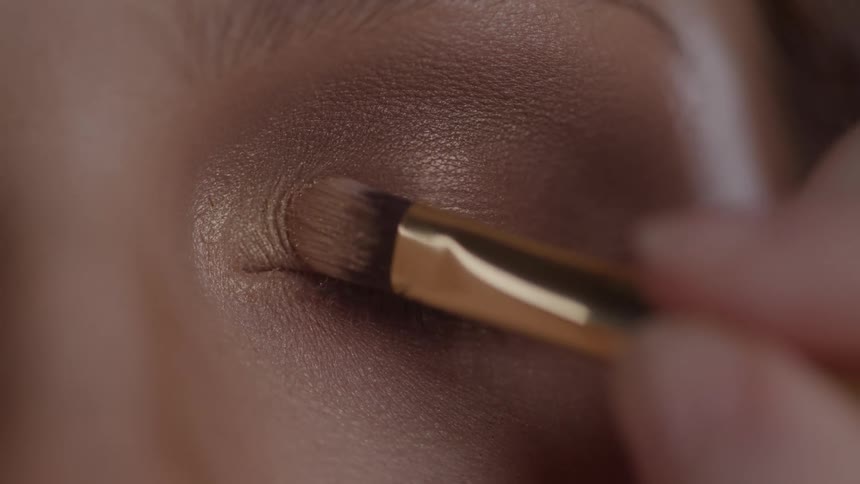Brush applies golden eyeshadow on closed eyelids