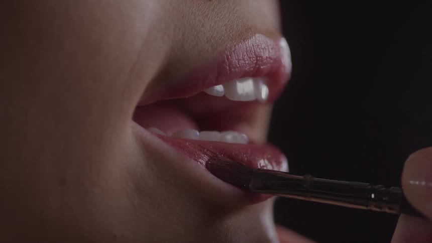 Dark lipstick being applied with a brush to a womans slightly parted lips