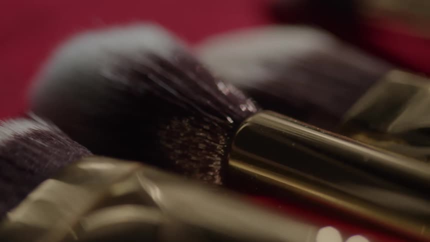 Makeup brushes with dark bristles and gold handles on a red surface