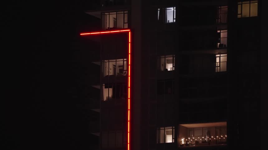 Modern building at night with red neon lights outlining the architecture and lit windows revealing interior spaces