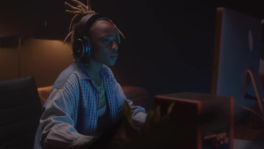 A young black woman working at a desk with a desktop computer in a music studio