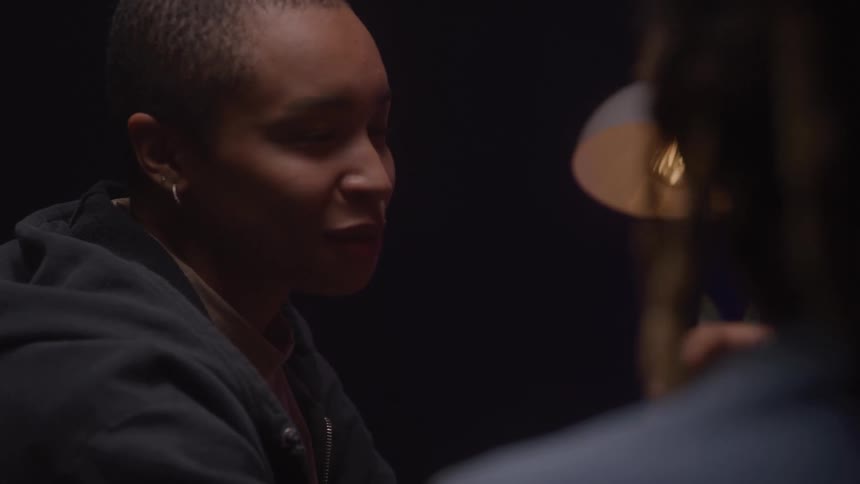 Two people talk in a setting lit by a lamp
