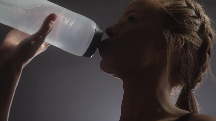 Close up of a young woman drinking water from a water bottle in a room