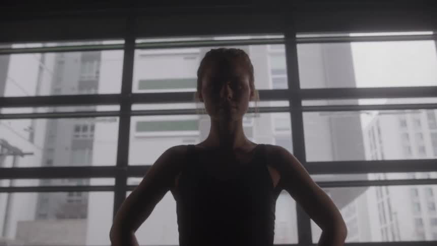 Person standing with hands on hips in front of a large window indoors