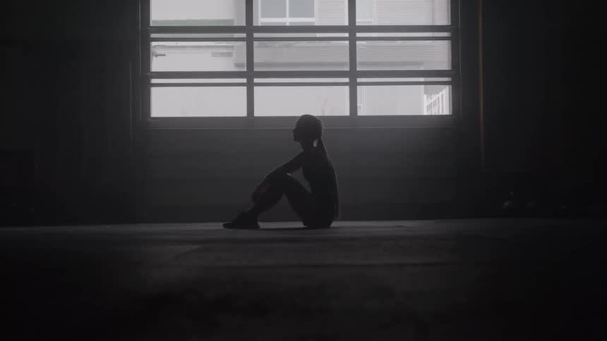 Woman sitting on the floor of a dim space in a contemplative pose before a large illuminated window