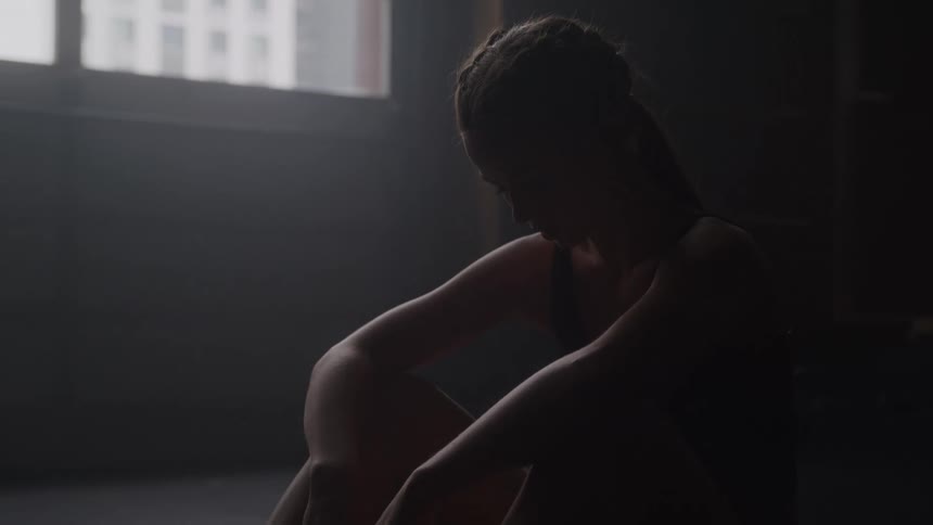 Woman sitting on the floor in a dark room with light coming through the window