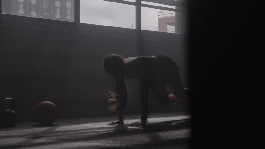 A woman works out in a dim gym with sunlight streaming through window