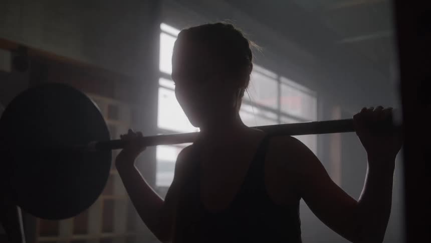 Person holding a barbell on their shoulders during a squat in an indoor setting