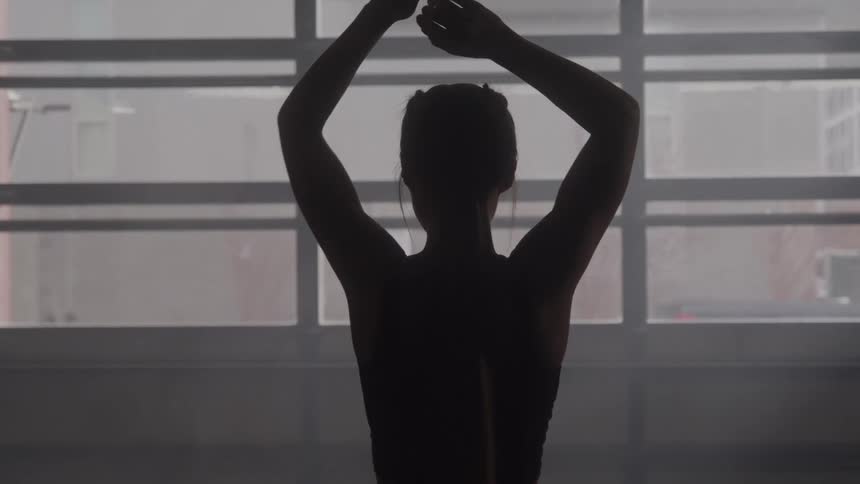 A silhouetted person stretches indoors against a large window