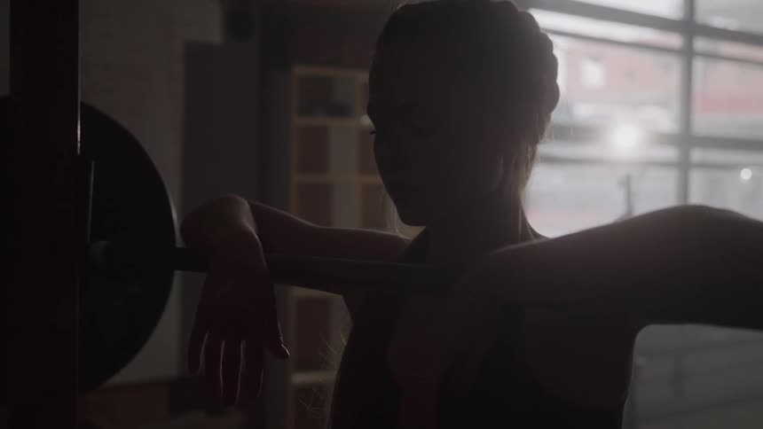 A woman is leaning with her hands on an exercise barbell in a gym
