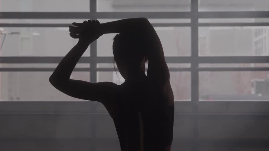 A silhouette stretching with arms overhead in a hazy gym posture focused and determined