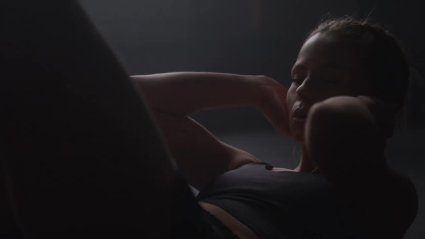 Woman performs abdominal exercises in a dark setting with soft lighting