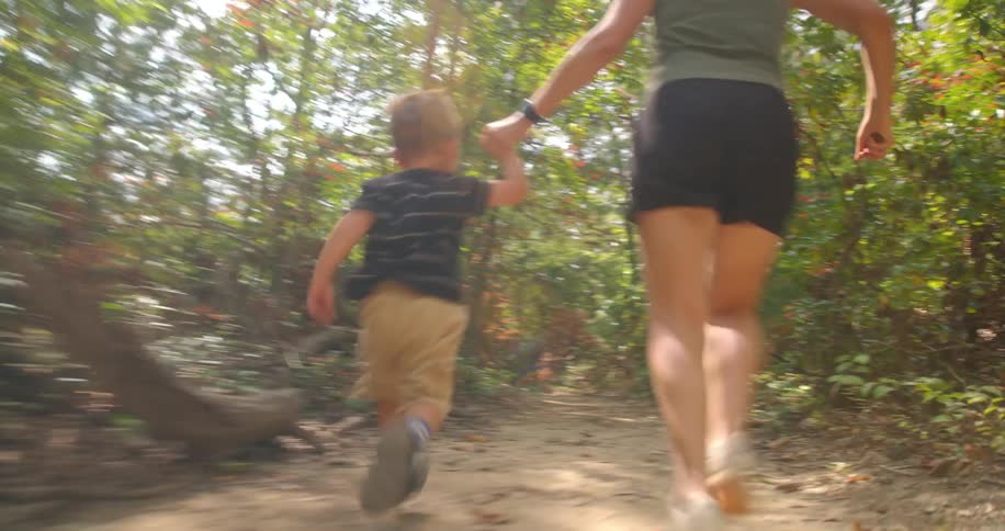 An adult and a small child run handinhand along a sunlit forest trail playful and energetic