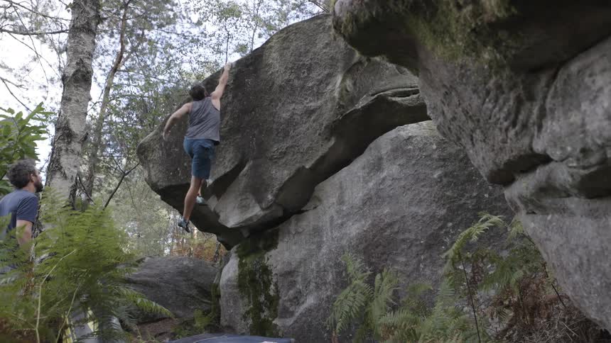 Man climbs a rock with support from a partner nearby
