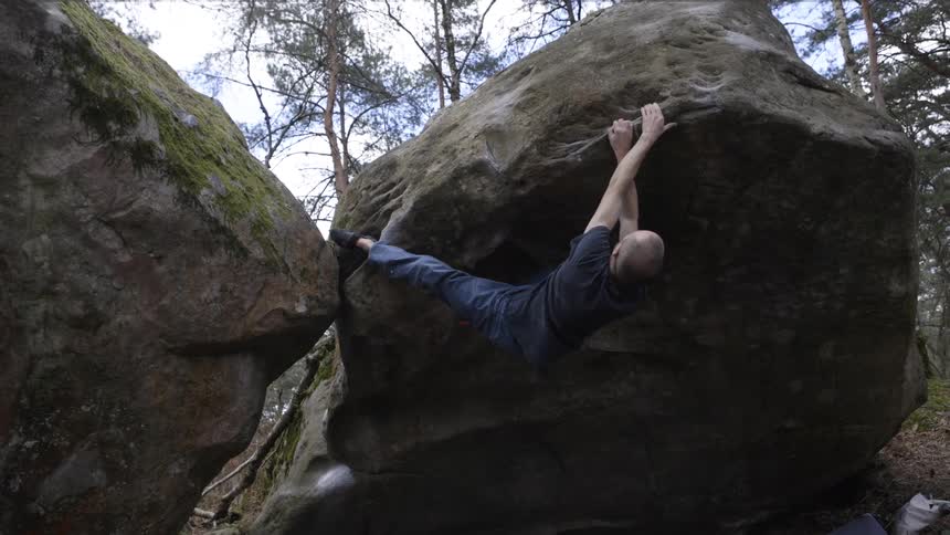 Climber stretches between two boulders heelhooked and arms extended while traversing an overhang