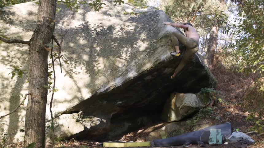 A man climbs a large boulder in the forest