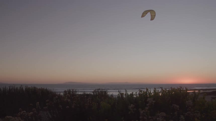 The kite is flying over the shore at sunrise